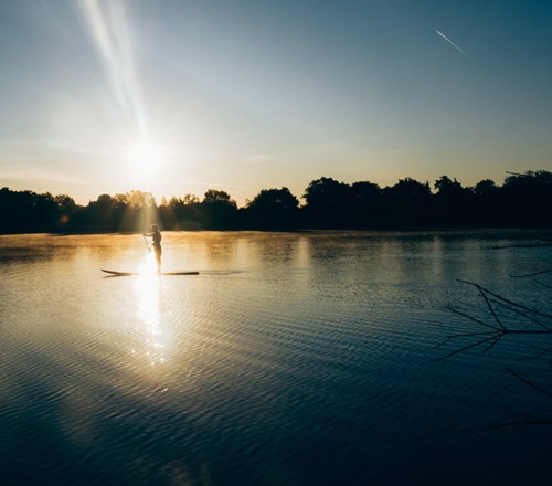 someone paddleboarding on a lake at sunset