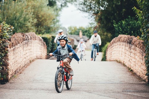 A child riding a bike on a bridge with family behind