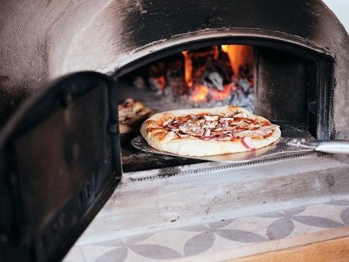 A woodfired pizza being brought out of the oven on a paddle